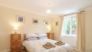 A bedroom with a large bed, two bedside tables, a chandelier, and a window with curtains. - Tiffany's Cottage (Great Yarmouth)