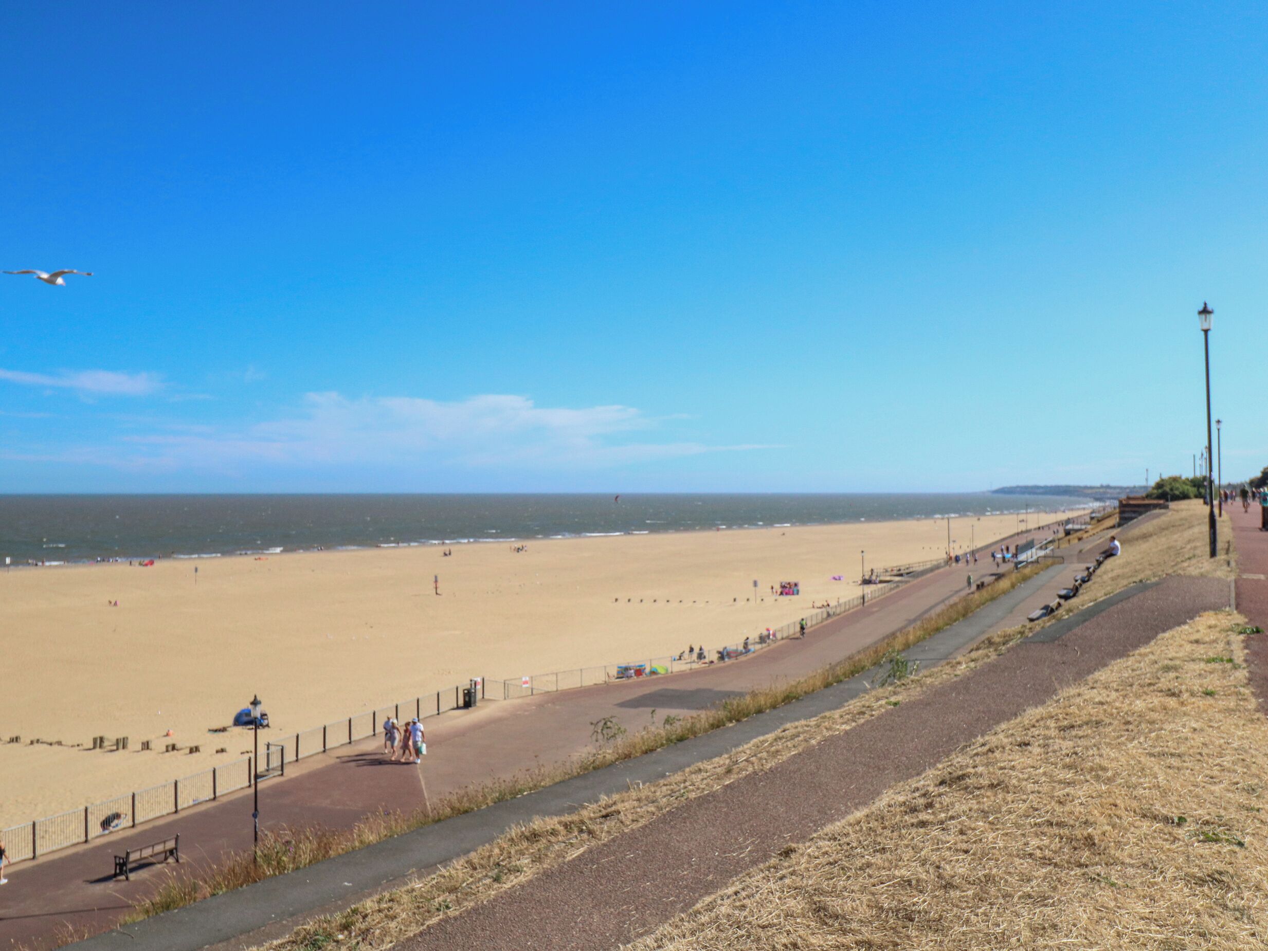 A beach with a paved walkway, benches, and a fence.