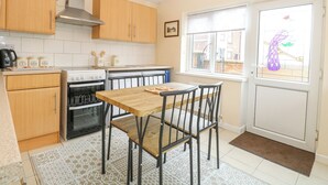 A compact kitchen with wooden cabinets, a gas stove, an oven, and a dining table with chairs. - Tiffany's Cottage (Great Yarmouth)
