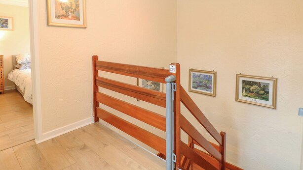 Een trap met houten leuningen die leidt naar een slaapkamer met een bed en nachtkastje.