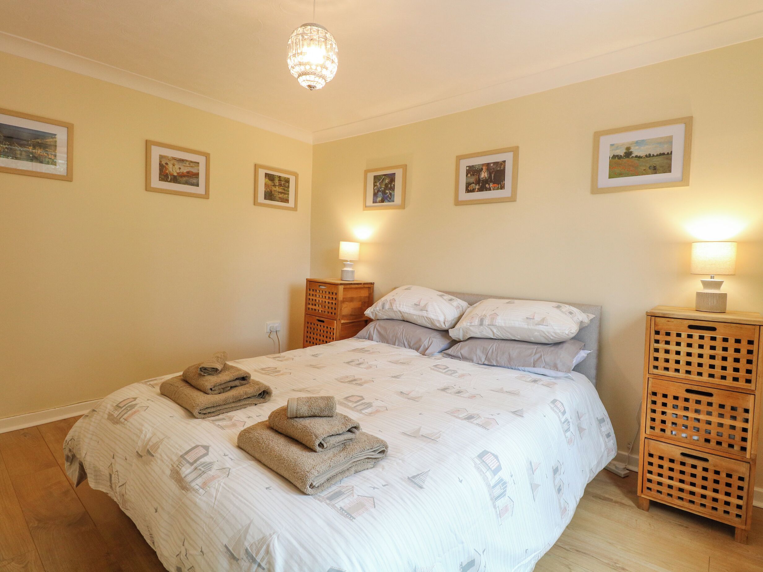 A neatly made bed with a patterned bedspread, two bedside lamps, a wooden nightstand, and a wall with framed pictures.