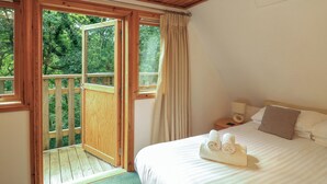 A bedroom with a wooden ceiling, a bed with white linens, a nightstand, and a view of greenery outside. - Lodge 58 - Oak Tree Lodge (Newton Abbot)