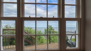 A room with a large window overlooking a garden and a body of water. - Rokeby House (Whitby)