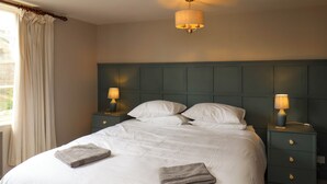 A neatly made bed with two pillows and two folded towels, flanked by two bedside tables with lamps, in a room with a dark headboard and a hanging light fixture. - Rokeby House (Whitby)