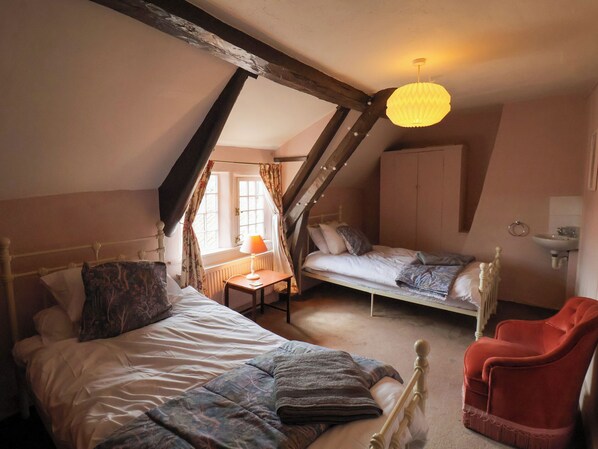 A bedroom with two beds, a red chair, a wooden ceiling, and a window with curtains. - Rokeby House (Whitby)