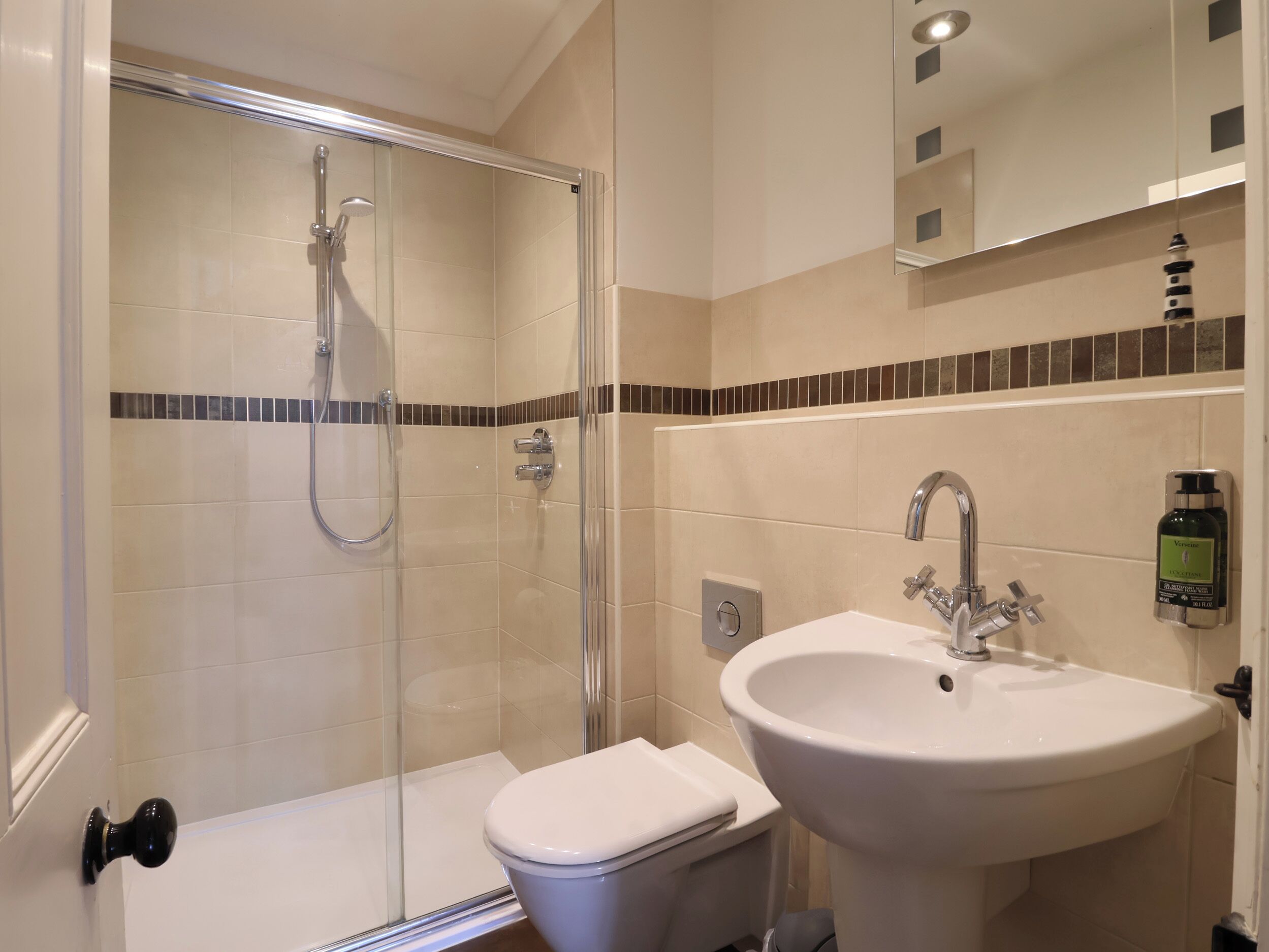 A bathroom with a glass-enclosed shower, a toilet, and a sink with a mirror above.