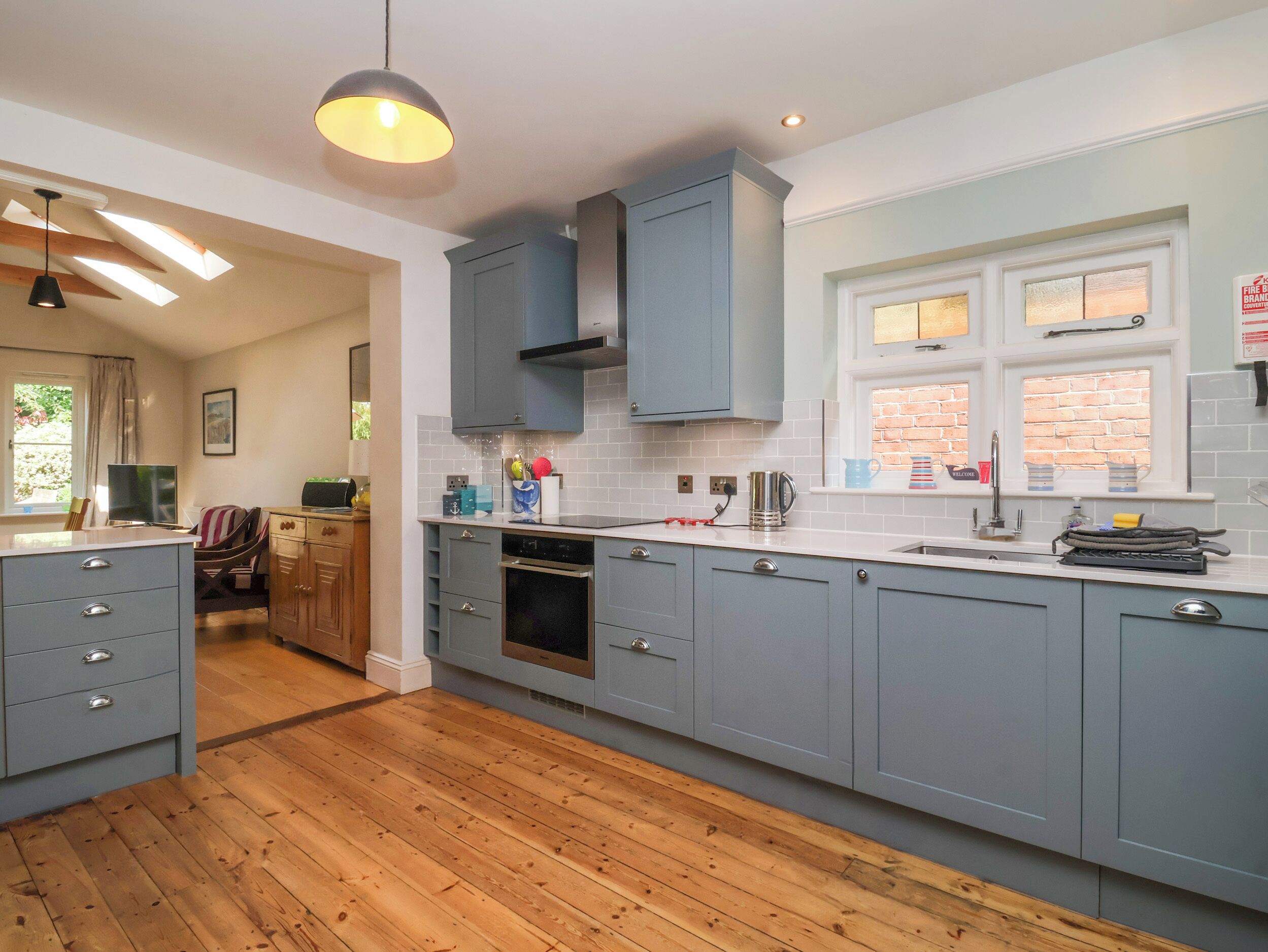 A modern kitchen with grey cabinets, a built-in oven, and a window with a brick wall view.