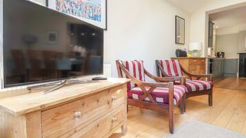 A living room with a flat-screen TV, wooden furniture, and a kitchen in the background.