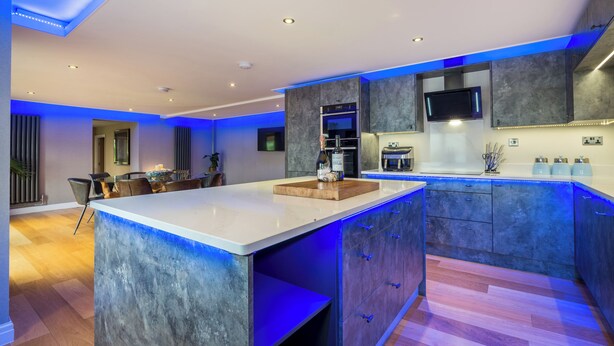 A modern kitchen with a large island, built-in appliances, and blue under-cabinet lighting. - Ullswater View House (Penrith)