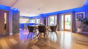 A modern kitchen with a central island, a dining area with a table and chairs, and large windows with curtains. - Ullswater View House (Penrith)