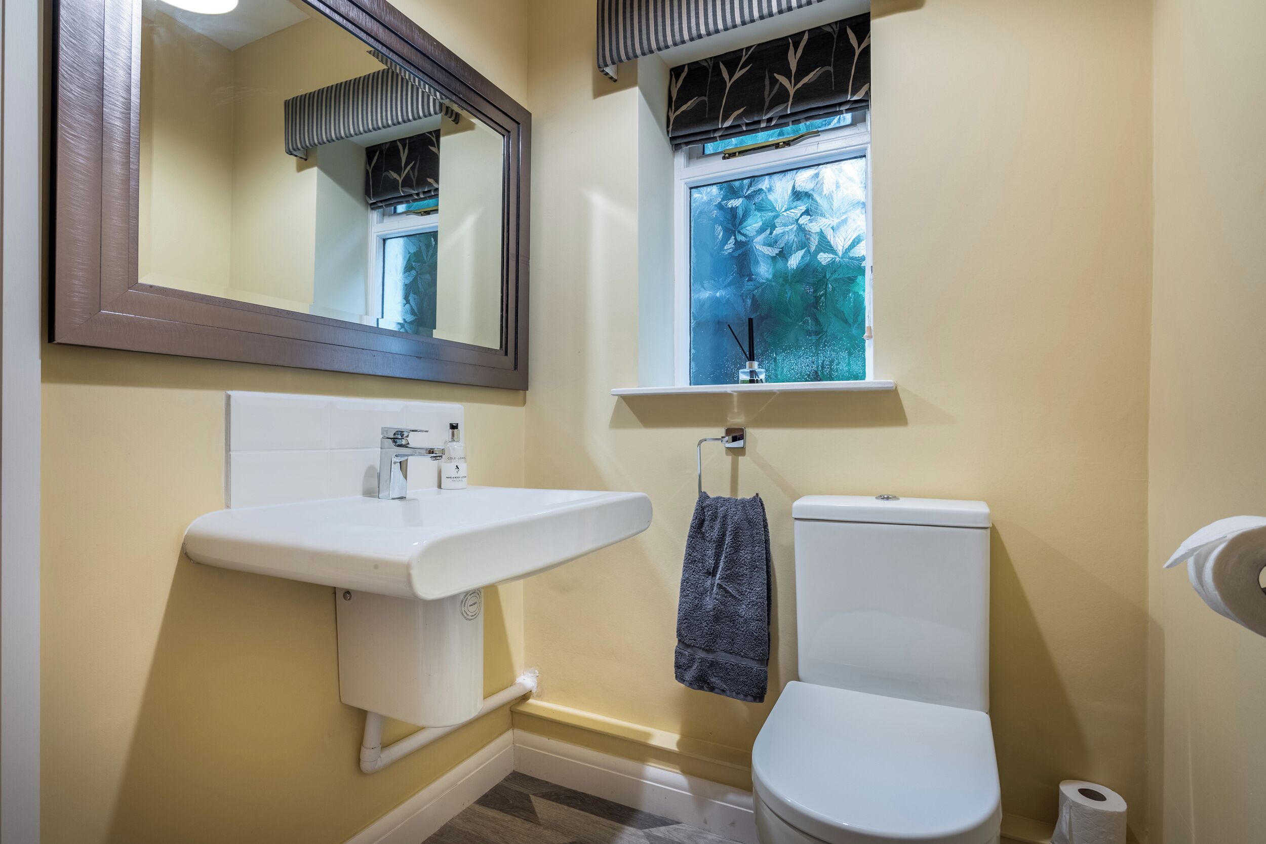 A bathroom with a white sink, a toilet, a window with a view of trees, and a mirror.