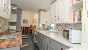 A compact kitchen with white cabinets, a microwave, a washing machine, and a dining area with a table and chairs. - Home From Home (Portland)