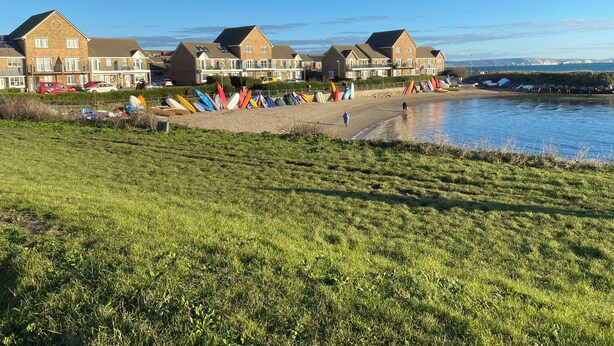 A coastal residential area with houses, a grassy field, and a beach with colorful kayaks. - Home From Home (Portland)