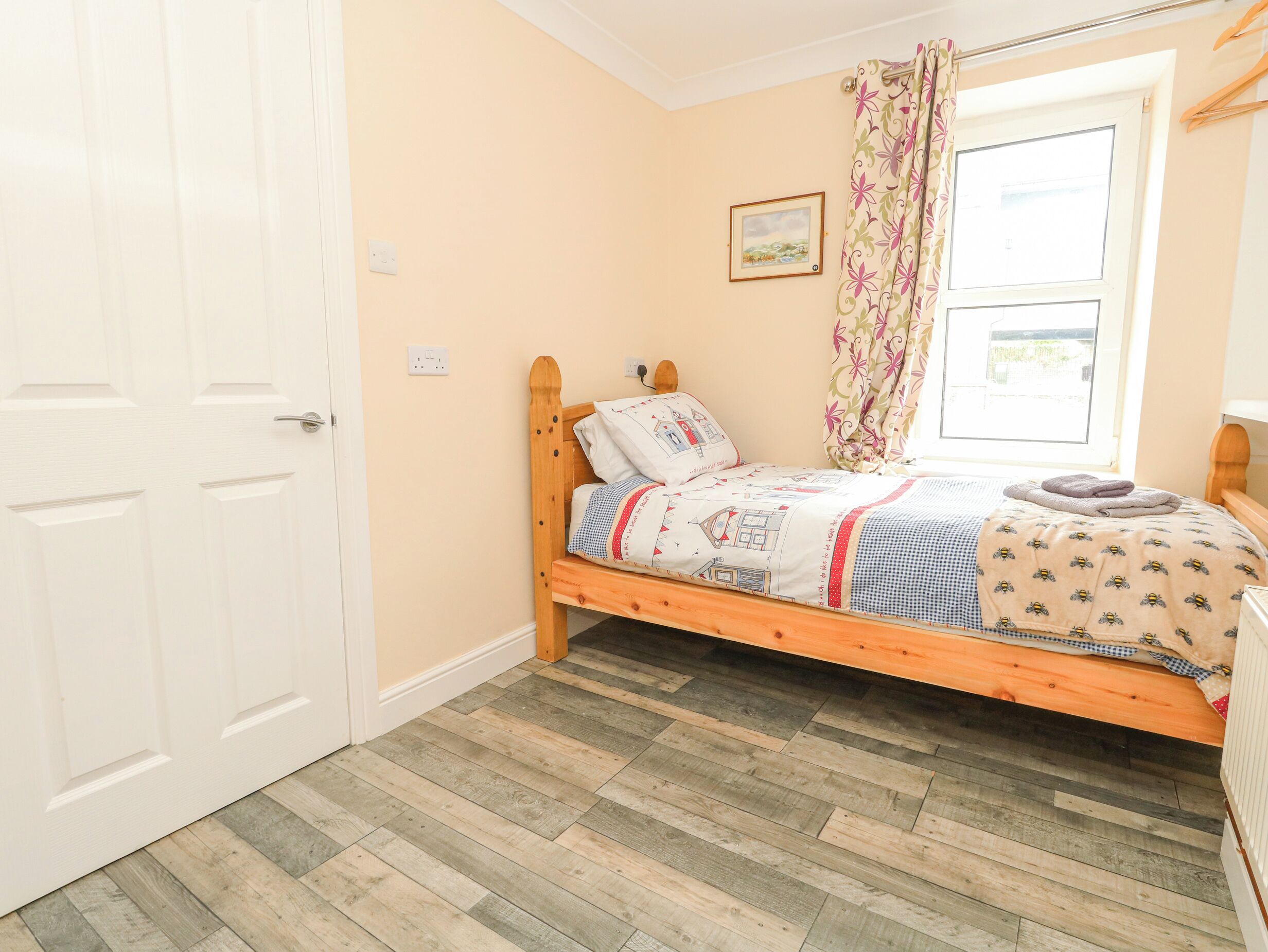 A single bed with a floral-patterned headboard, a wooden floor, and a window with a curtain.