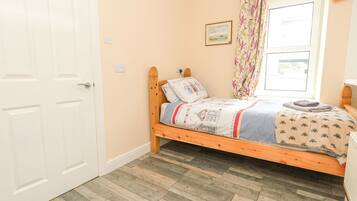 A single bed with a floral-patterned headboard, a wooden floor, and a window with a curtain.
