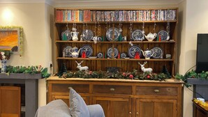 A living room with a wooden bookshelf filled with books and decorative plates, a sofa with cushions, and a television on a stand. - Home From Home (Portland)