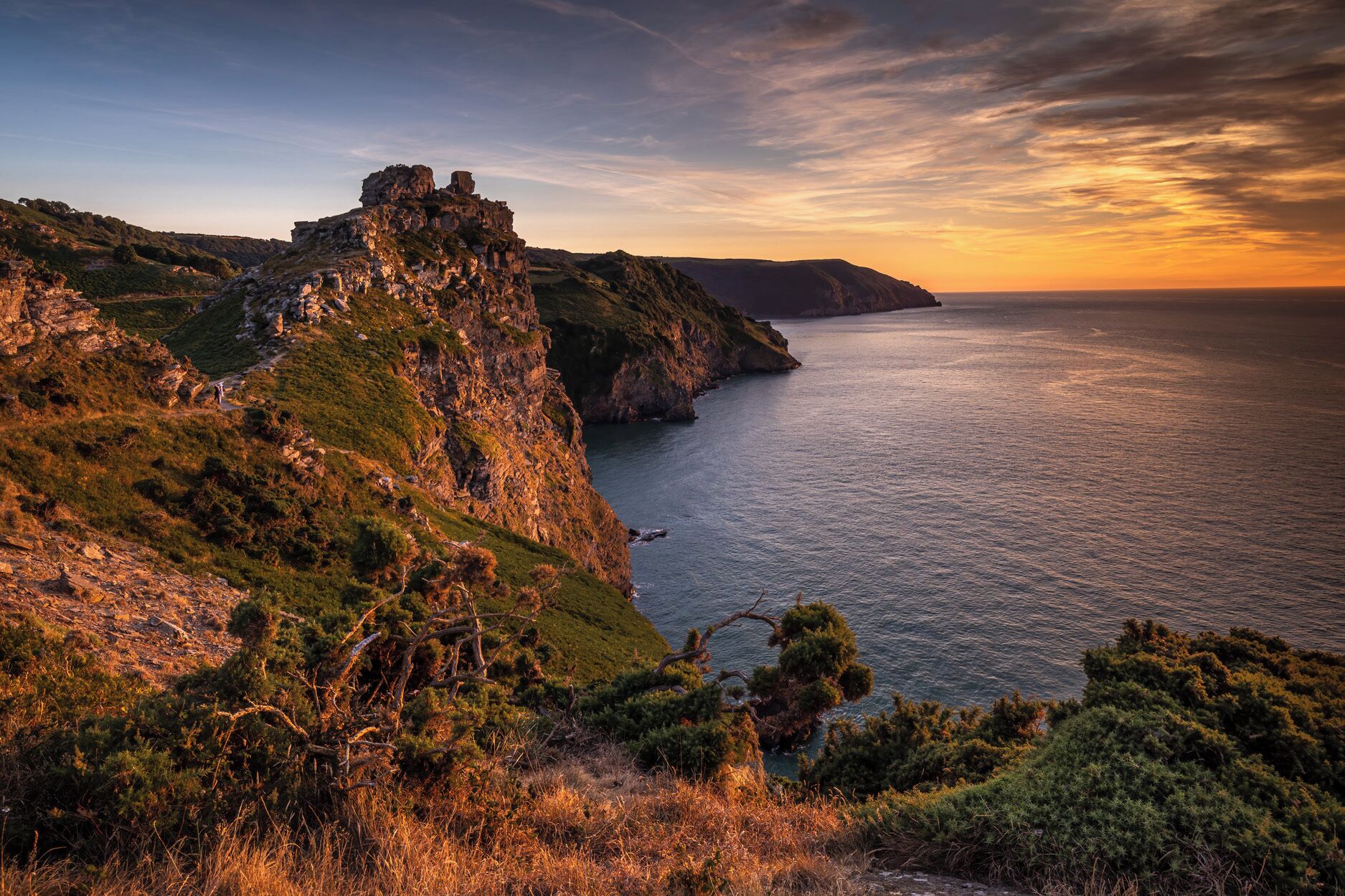 A coastal landscape with a rocky cliff and a small building on top.