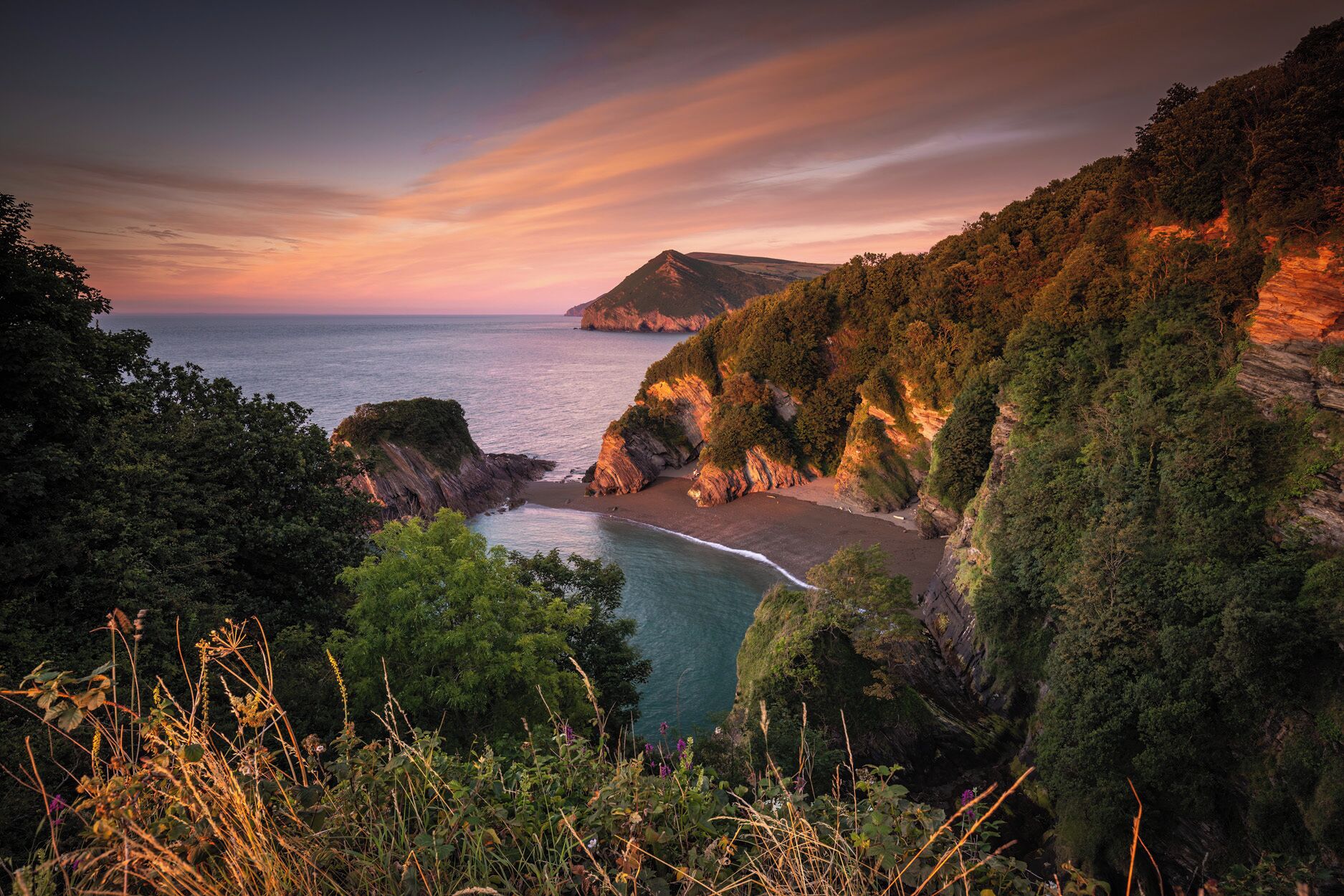 A coastal landscape with cliffs, a beach, and a mountain in the distance.