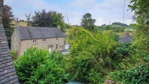 A stone house with a sloped roof, surrounded by lush greenery and a clear sky.