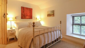 A bedroom with a bed, two bedside tables, a hanging lamp, a window with blinds, and artwork on the walls.