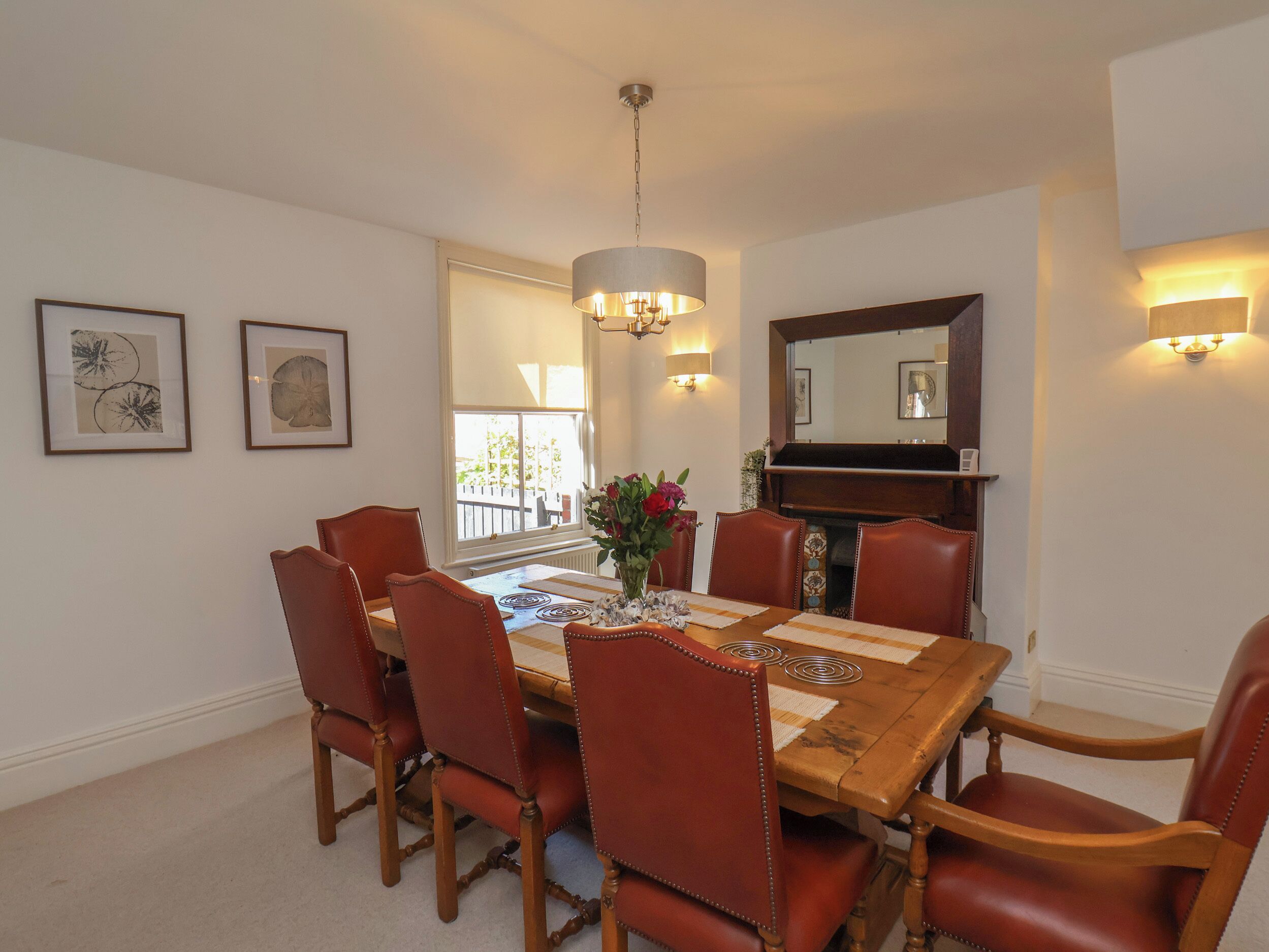 A dining room with a wooden table and leather chairs, a chandelier, wall-mounted sconces, and framed artwork.