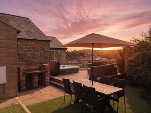 A patio with a stone fireplace, outdoor seating, and a view of the countryside at sunset. - Barncroft (Matlock)