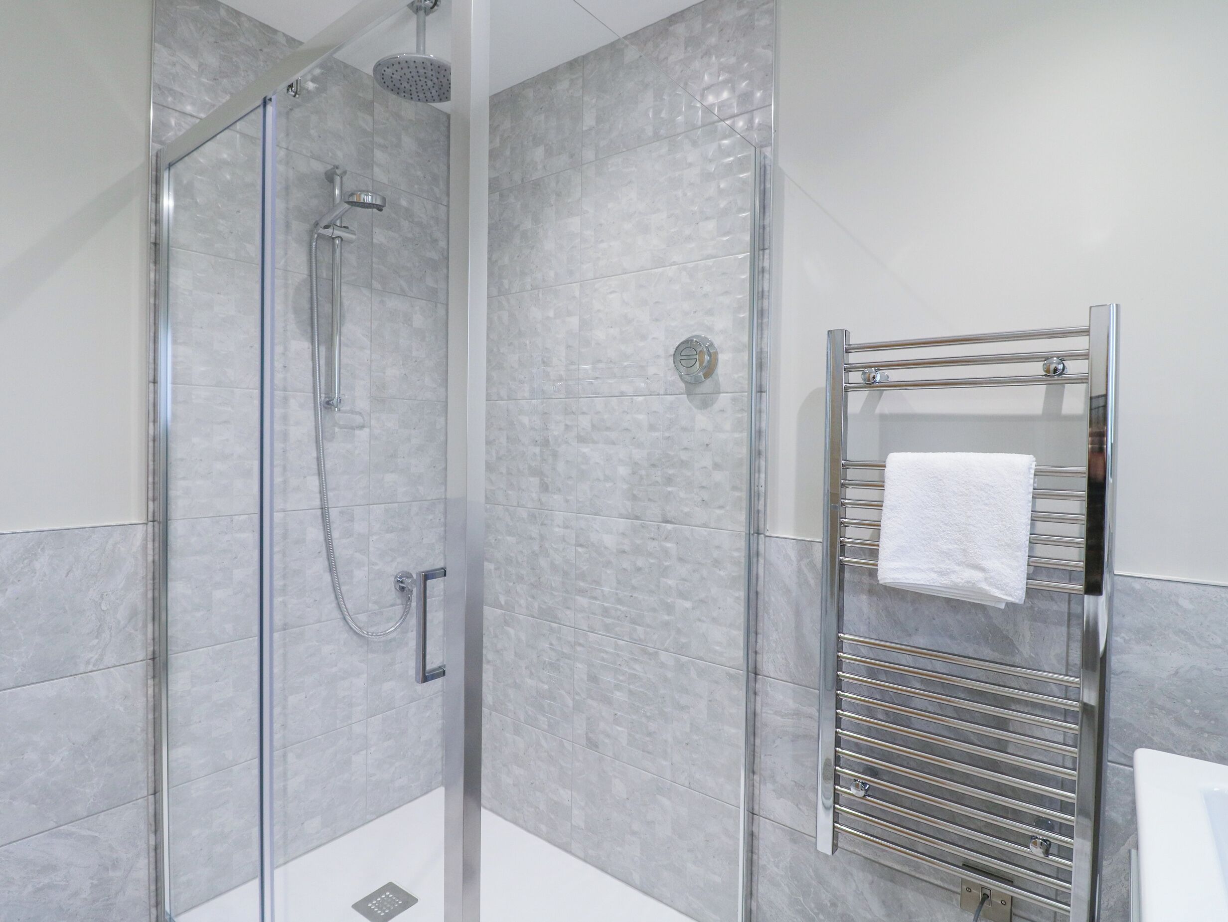 A modern bathroom with a glass-enclosed shower, a chrome towel rack, and grey marble tiles.