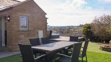 A patio with a table and chairs, a barbecue grill, and a view of the countryside.
