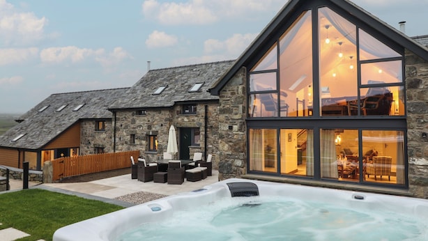 A modern house with a stone exterior, a large glass conservatory, and a hot tub in the foreground. - Y Côr (Corwen)