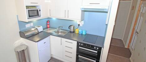 Une cuisine de taille réduite, dotée de meubles blancs, d’un four à micro-ondes, d’un grille-pain, d’un évier et d’un lave-vaisselle.