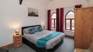 Une chambre à coucher avec un lit, une table de chevet, une armoire en bois et une fenêtre avec des rideaux.
