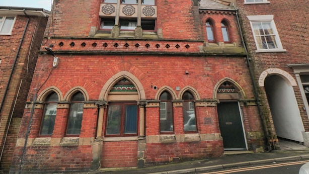 Un bâtiment en briques rouges, doté de fenêtres en arc de cercle et d’une enseigne indiquant « Maison de l’église ».