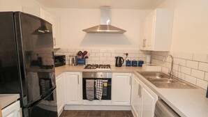 Une cuisine de taille réduite avec des meubles blancs, un réfrigérateur noir, une cuisinière et un lave-vaisselle.