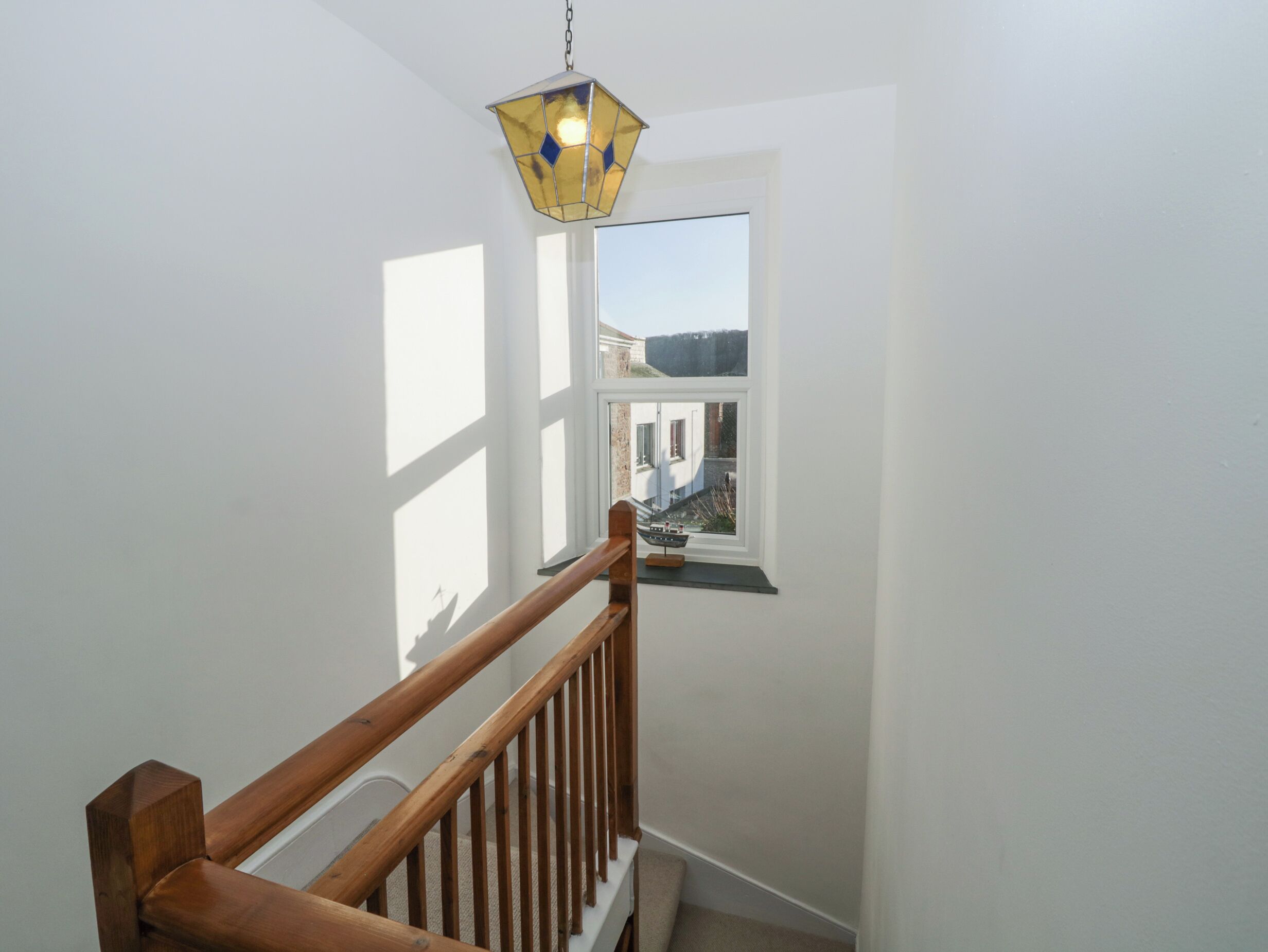 A staircase with a wooden handrail and a small window with a view of a building and a boat outside.