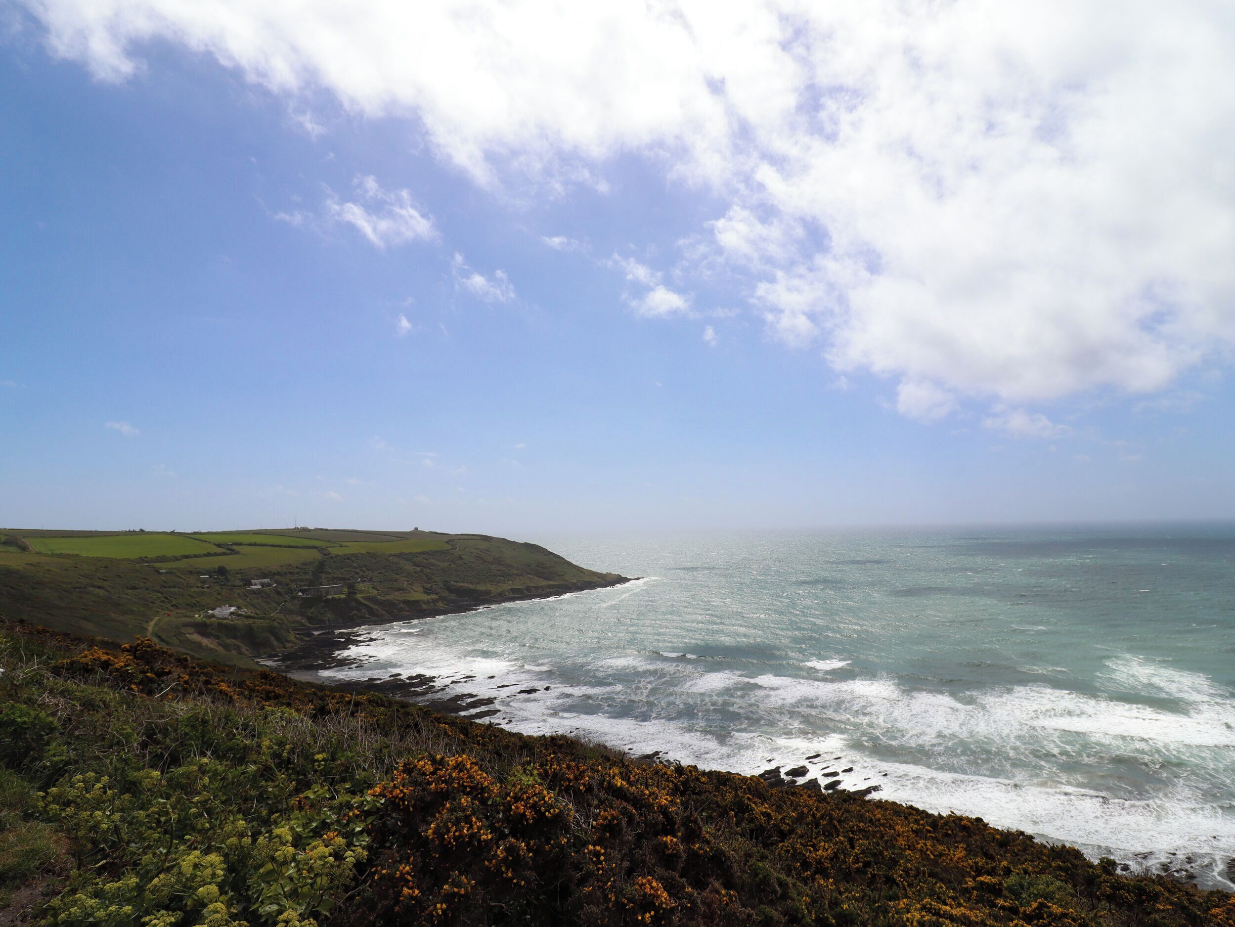 A coastal landscape with a view of the sea and a grassy hill.