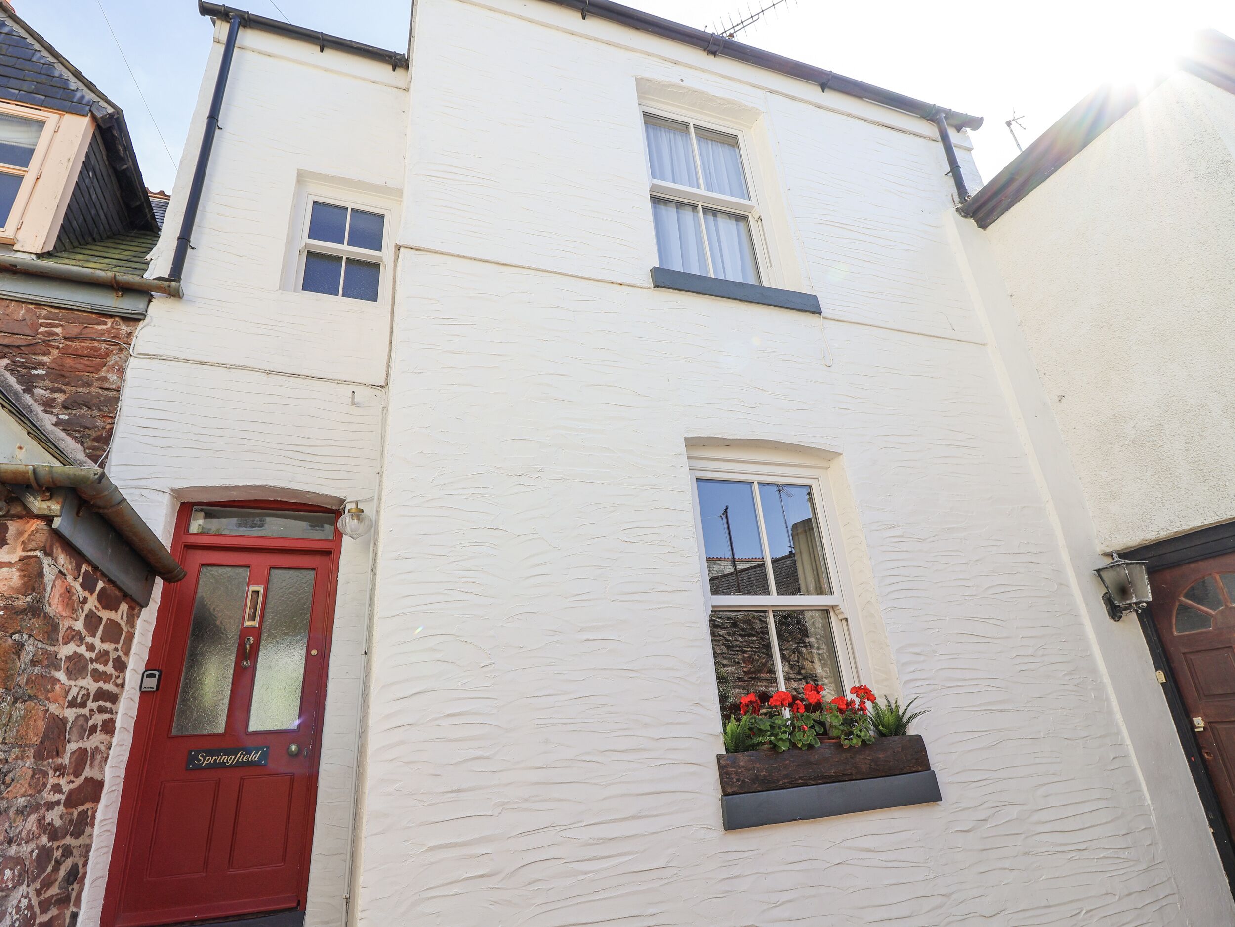 A two-story building with a red door labeled "Springfield," a window with red flowers, and a brick wall on the left.