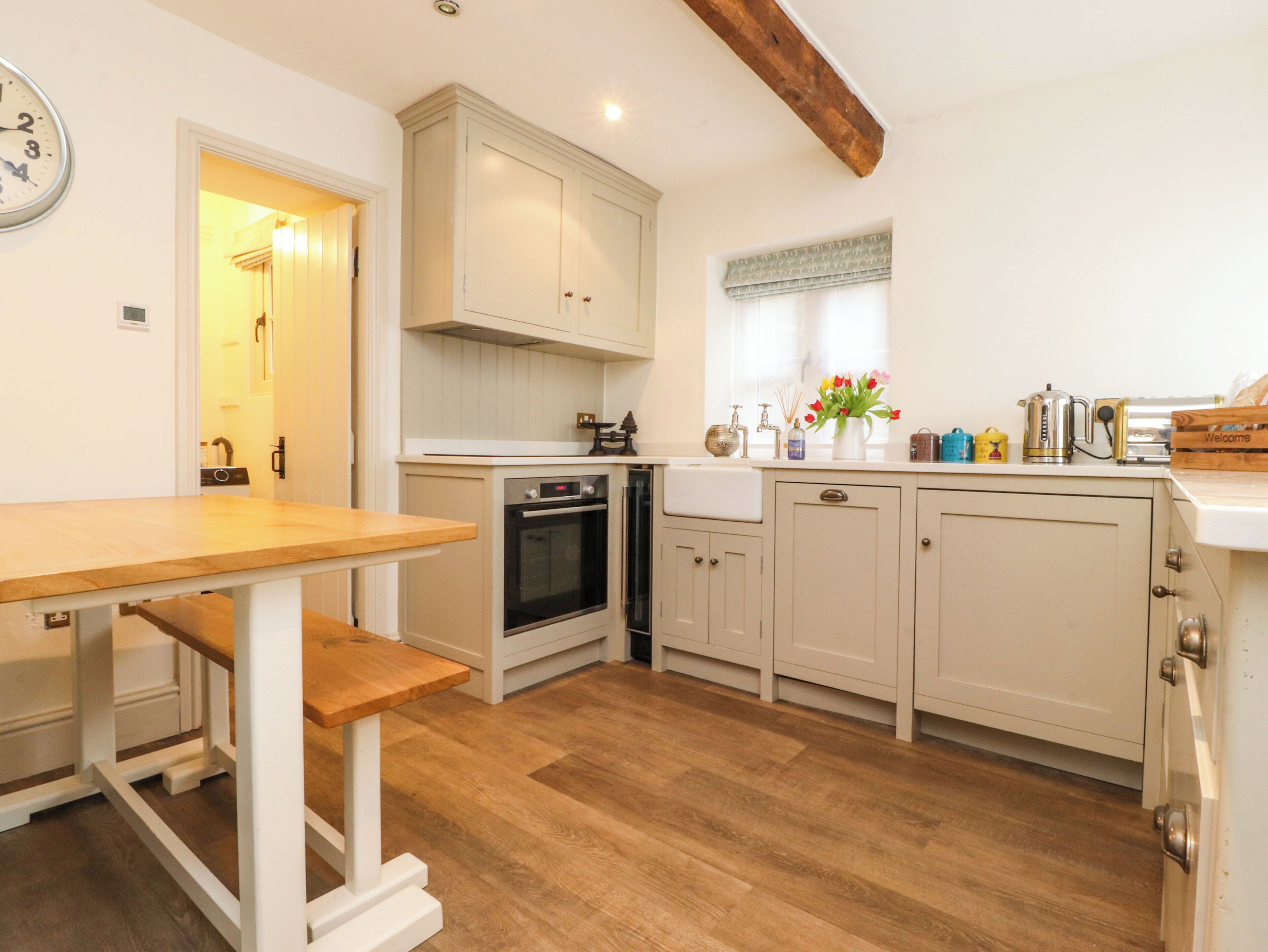 A kitchen with wooden flooring, white cabinetry, a built-in oven, and a wooden table.