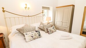 A neatly made bed with white linens and decorative pillows, a wooden nightstand, a bedside lamp, and a wardrobe with a mirror. - The Old Cobblers (Skipton)