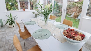 A dining area with a long table set for two, surrounded by chairs, with a view of the garden through large windows. - Kerangarth (Corbridge)