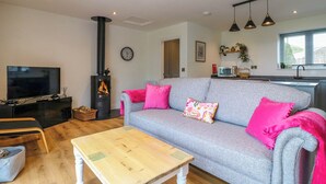 Ein gemütliches Wohnzimmer mit grauem Sofa, Couchtisch aus Holz und einem schwarzen Kaminofen.