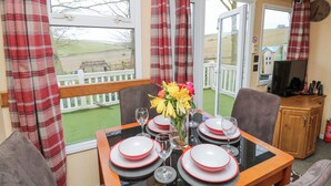 A dining area with a table set for four, a vase with flowers, and a view of the outdoors through large windows. - Rowborough House (Newport)