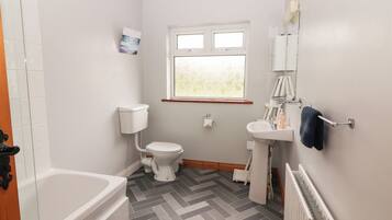 A small, clean bathroom with a toilet, sink, and bathtub. There is a window providing natural light and a radiator on the wall.