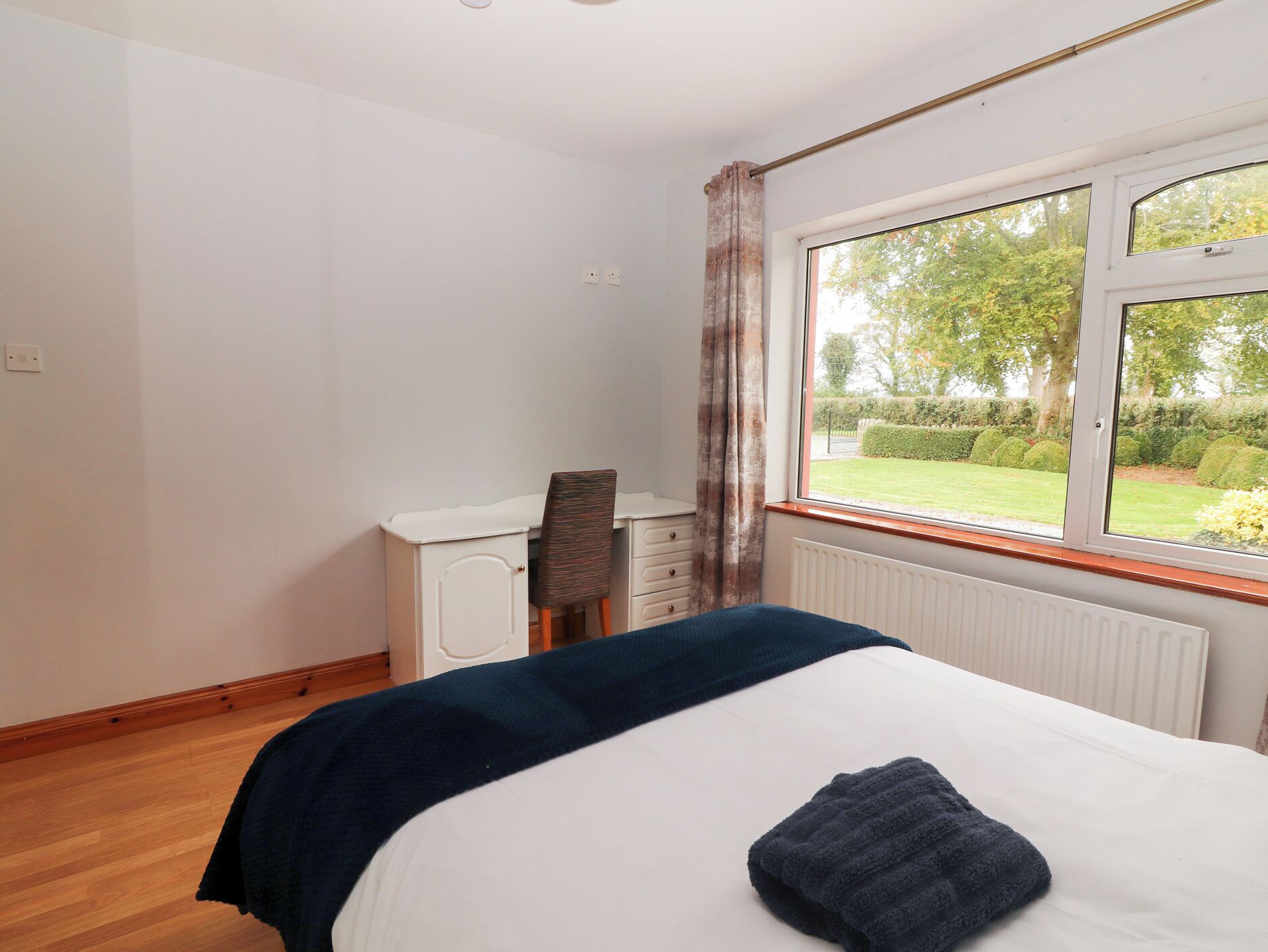 A bedroom with a bed, a desk, and a window with a view of a garden.