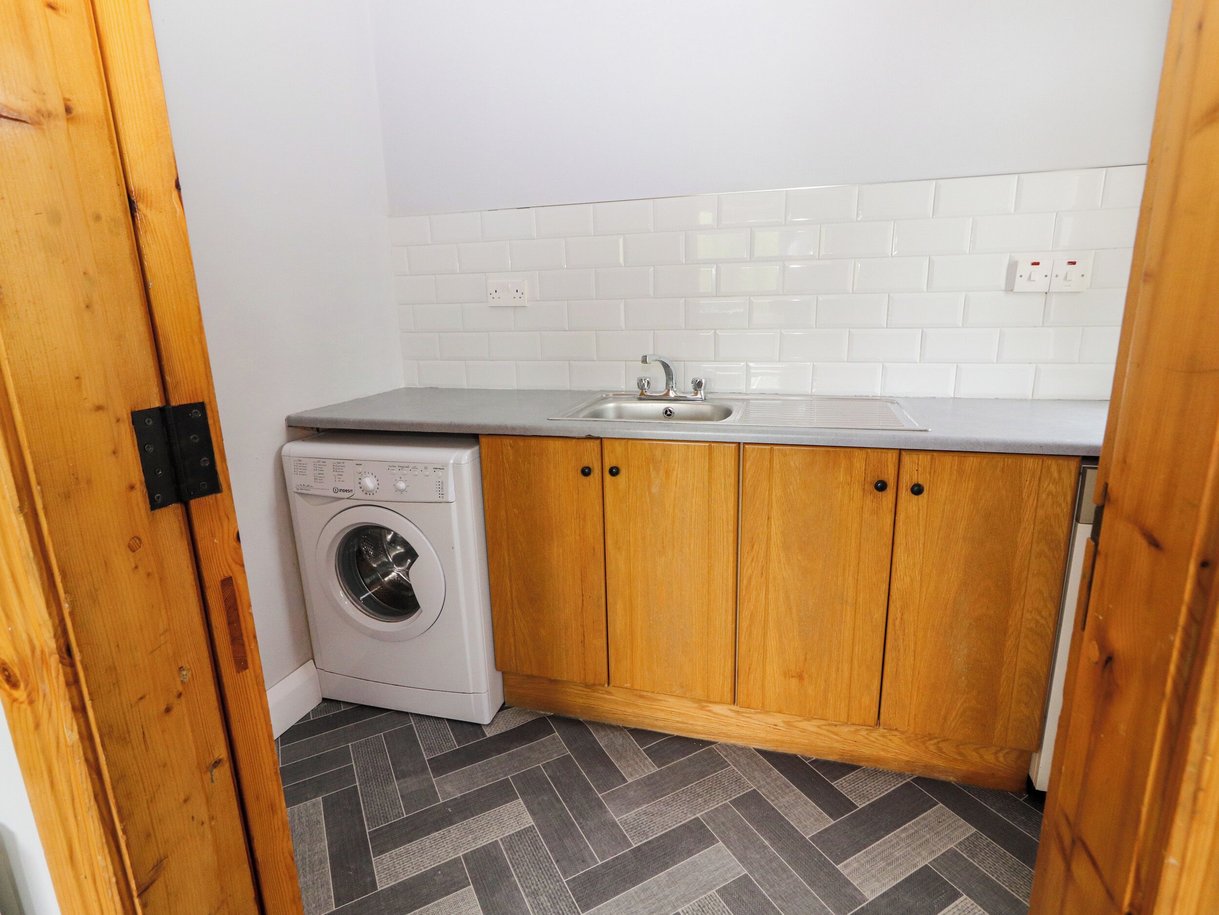 A compact kitchen with a washing machine, wooden cabinets, and a tiled backsplash.