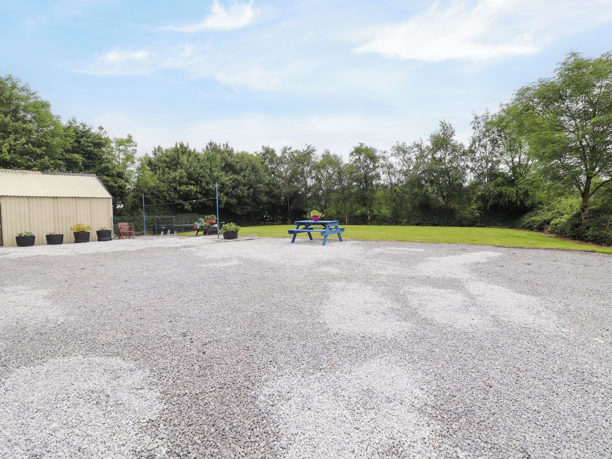 A gravel parking area with a blue picnic table and potted plants.