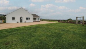 A white house with a sloped roof, a front porch, and a driveway leading to the entrance. - Cois Leice (Mulranny)