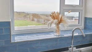 A kitchen with a window overlooking a rural landscape, a vase with dried plants, and a stainless steel sink. - Coastguard View (Portland)