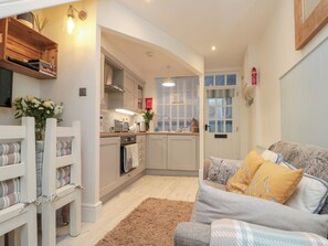 Un espacio habitable compacto con kitchenette, un sofá con cojines estampados y un pequeño banco de madera.