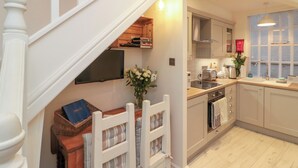A modern kitchen with a built-in oven, a sink, and a dining area with a white chair and a basket. - Little Gem (Whitby)