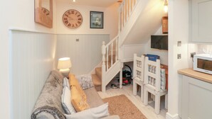 A cozy living room with a sofa, a lamp, a staircase, and a kitchen area. - Little Gem (Whitby)